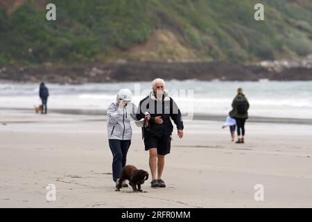 Promeneurs de chiens sur la plage de Carne en Cornouailles, comme un avertissement de danger pour la vie a été émis alors que la tempête Antoni frappe certaines parties du Royaume-Uni, apportant de fortes pluies et des vents forts. Date de la photo : Samedi 5 août 2023. Banque D'Images