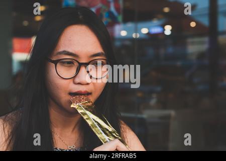 Gros plan jeune femme heureuse mordant une barre de chocolat. Concept de nourriture de style de vie des gens Banque D'Images