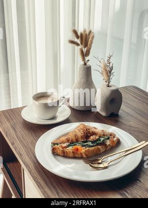 Croissant avec saumon et œufs brouillés avec café sur une table basse Banque D'Images