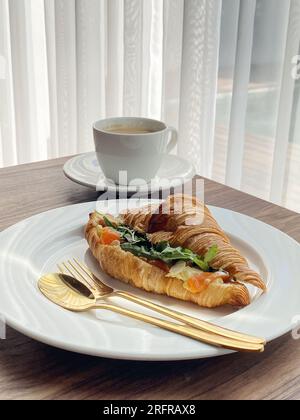 Croissant avec saumon et œufs brouillés avec café sur une table basse Banque D'Images
