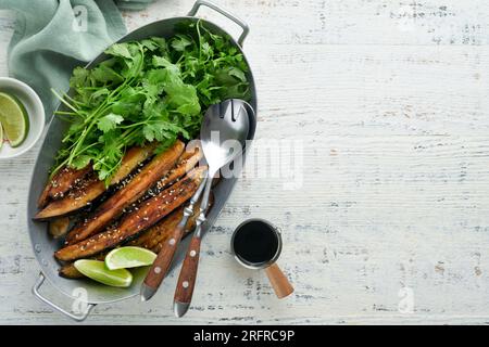 Tranches d'aubergines grillées ou cuites au four dans de la farine de riz, avec coriandre et sauce soja sur fond de table rustique en bois blanc. Vue de dessus avec espace de copie. Banque D'Images