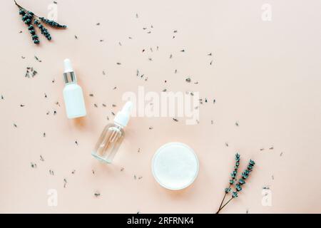 Sérum cosmétique naturel lavande, huile essentielle et pot de crème sur fond beige pastel avec des fleurs. Aromathérapie, concept cosmétique de soin de la peau. Haut vi Banque D'Images