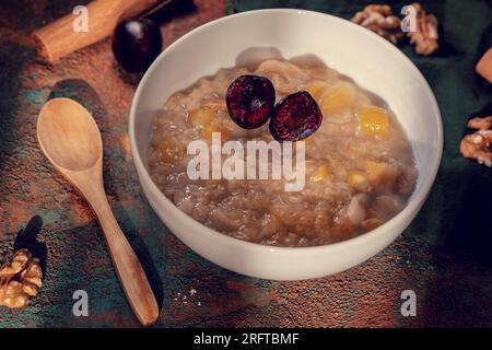 Dessert turc traditionnel appelé «aşure» dans un bol en céramique avec une cuillère en bois sur un fond en bois brun gros plan, photographie de nature morte Banque D'Images