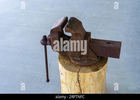 Ancienne pince d'étau rouillée montée sur une souche de bois avec un fond en béton. Howard Iron Works, Buffalo, New York. Banque D'Images