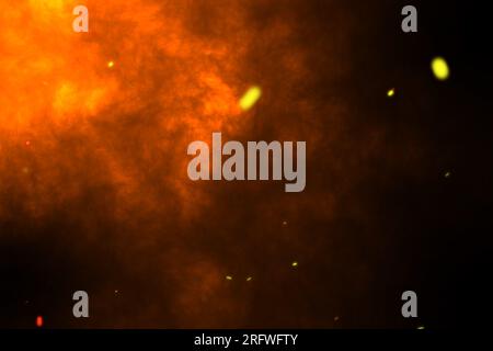 Étincelles orange brûlantes se lèvent du feu, particules de feu sur fond rouge. Banque D'Images