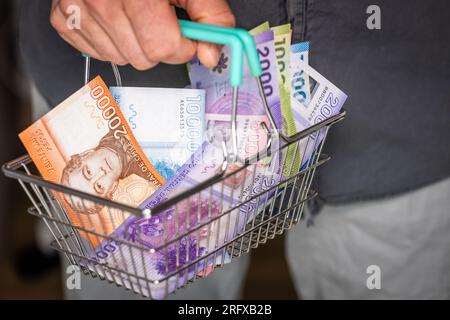 Chili argent dans le panier. Un homme tenant un panier avec de la monnaie pesos chiliens dans sa main, concept financier et économique. Hausse des prix, baisse p Banque D'Images