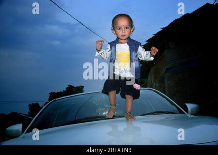 Heureuse petite fille sur la grande voiture blanche ayant du plaisir à regarder la caméra. Repos en vacances dans la campagne en plein air Banque D'Images