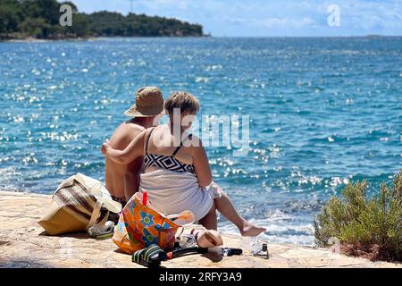 Porec, Kroatien. 06 août 2023. Plava Laguna, côte Adriatique près de Porec/Croatie, plage. Vacanciers, couple, couple sur la plage de pierre, plage rocheuse. ? Crédit : dpa/Alamy Live News Banque D'Images