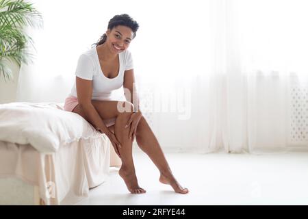 Belle jeune femme noire touchant sa jambe avec la peau soyeuse après l'épilation Banque D'Images
