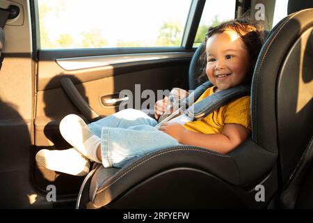 Joyeuse fille asiatique tout-petit assise dans le siège de bébé dans le véhicule Banque D'Images