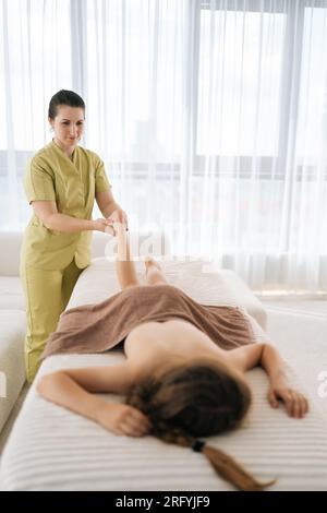 Tir vertical à distance de masseur féminin professionnel faisant des exercices orthopédiques de jambe de l'adolescente cliente, prévention de la douleur dans le talon, couché sur Banque D'Images