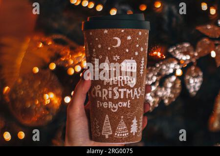 Main féminine tenant une tasse de café ou de thé avec un design créatif de Noël. Décor de vacances d'hiver, guirlande dorée du nouvel an Banque D'Images