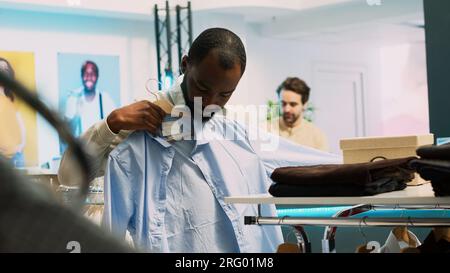 Client de détail masculin ramassant des vêtements dans des étagères, regardant la marchandise de grand magasin à acheter à prix réduit. Jeune adulte visitant le centre commercial en tant que client, activité commerciale. Prise de vue à main levée. Banque D'Images