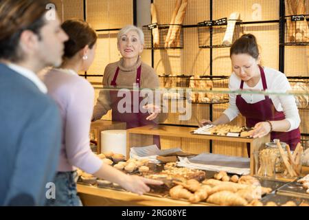 Des boulangers féminins souriants dans des tabliers marrons qui travaillent derrière le comptoir Banque D'Images