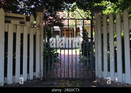 Un portail en fer forgé et une clôture blanche encadrent l'entrée du jardin d'une charmante maison de style Fédération australienne. Banque D'Images