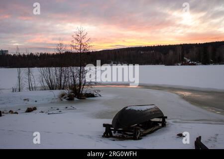 Une scène tranquille de Kuopio, Finlande avec un bateau à l'envers sur un lac gelé et Rosy Sunset Landscape Banque D'Images