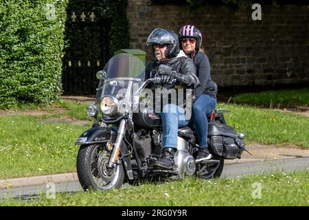 Whittlebury, Northants., Royaume-Uni - 6 août 2023. Homme et femme conduisant une moto Harley Davidson à travers un village anglais. Banque D'Images