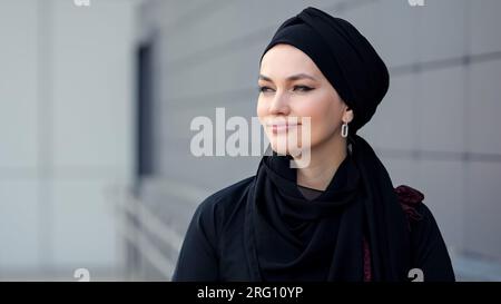 Femme musulmane en hijab noir marchant devant un bâtiment gris Banque D'Images