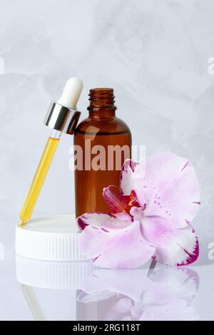 Gros plan du sérum du visage. Flacon en verre avec pipette. Huile de massage aromatique sur fond de marbre gris et fleur d'orchidée. Cosmétique spa biologique naturel, peau Banque D'Images