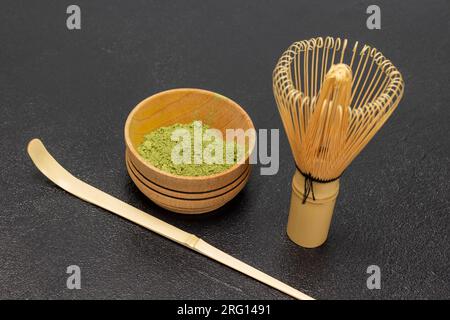 Thé vert Matcha en poudre dans un bol en bois. Fouet et cuillère en bambou sur la table. Vue de dessus. Fond noir Banque D'Images