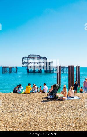 Les gens assis sur la plage par une chaude journée d'été avec le West Pier brûlé en arrière-plan, Brighton, Royaume-Uni Banque D'Images