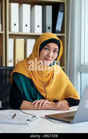 Portrait d'une femme d'affaires musulmane en hijab jaune assise à son bureau Banque D'Images