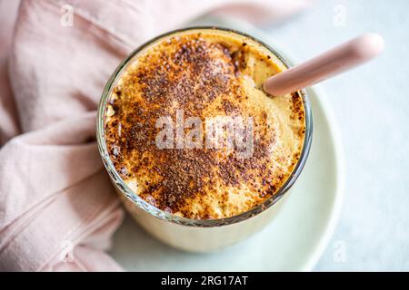 Vue de dessus de la tasse en verre avec dessert à la crème de café avec poudre de chocolat et glace servi sur une assiette avec cuillère et serviette pour le repas d'été rafraîchissant contre Banque D'Images