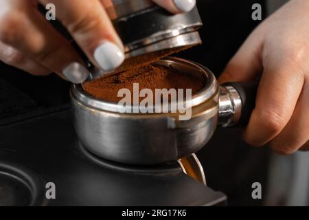 Le barista récolte anonymement du café aromatique moulu dans le porte-filtre sur le tapis d'inviolabilité pendant qu'il travaille au comptoir Banque D'Images