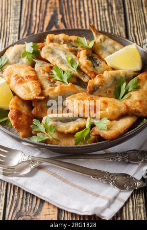 Anchois frits servis avec citron et herbes en gros plan sur une assiette sur la table. Vertical Banque D'Images