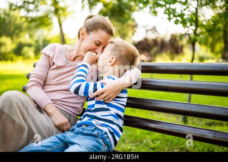 Mère heureuse est assise avec son fils sur le banc dans le parc. Ils s'amusent ensemble. Banque D'Images