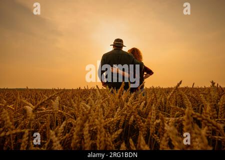 L'homme et la femme sont debout dans leur champ agricole au coucher du soleil. Ils cultivent du blé. Banque D'Images