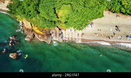 Vue aérienne de dessus de la plage de sable de drone au coucher du soleil. Paysage tropical avec des palmiers, des arbres et des gens se reposant sur le bord de mer. Banque D'Images