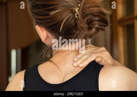 Une jeune fille tient sa main sur son cou à cause de maux de dos à la maison, maux de dos Banque D'Images