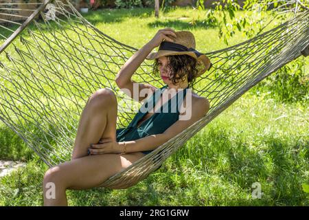 Fille allongée sur une chaise longue en été avec un chapeau regardant devant Banque D'Images