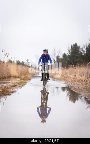 Garçon chevauchant son vélo de montagne à travers une flaque d'eau sur un sentier inondé. Banque D'Images