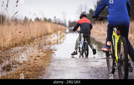 Deux garçons à vélo à travers une grande flaque d'eau sur un sentier inondé. Banque D'Images