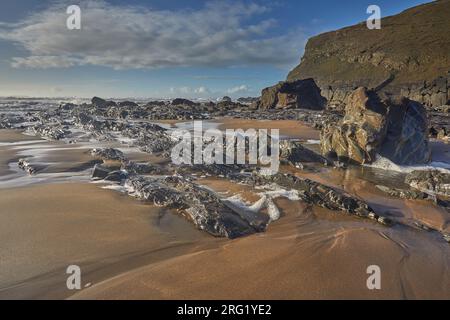 Un bord de mer sablonneux parsemé de roche adossé à une puissante falaise, dans une crique appelée Duckpool, près de Bude, sur la côte atlantique des Cornouailles, en Grande-Bretagne. Banque D'Images