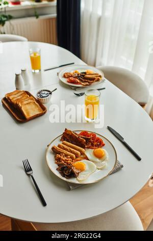 Vue à angle élevé du petit déjeuner avec des œufs au plat et des saucisses près des couverts et du jus d'orange à la maison Banque D'Images