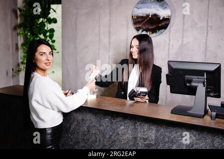 Un jeune concierge sympathique se tient derrière un comptoir de réception et donne des informations sur la chambre aux clients qui se trouvent dans un hôtel. Banque D'Images