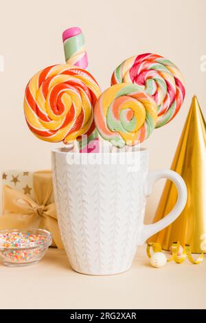 Bonbons colorés dans une tasse sur une table sur fond clair. Grands sucettes tournantes. Concept créatif d'un pot rempli de délicieux bonbons de la Banque D'Images