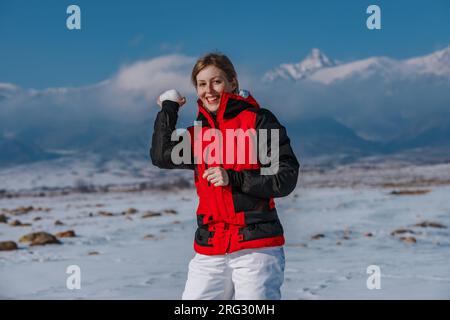 Jeune femme jetant une boule de neige sur fond de montagne Banque D'Images