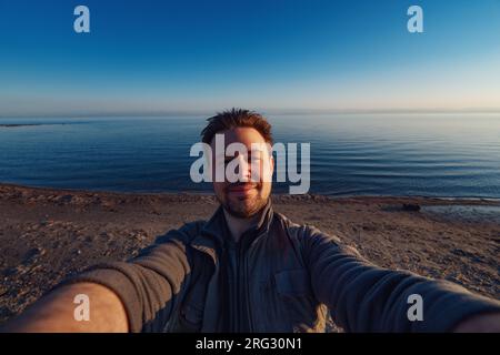 Heureux jeune homme selfie devant le lac, grand angle de vue Banque D'Images