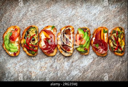 Ensemble de bruschetta assorties avec diverses garnitures pour les vacances sur la planche de pierre. Vue de dessus. Concept de nourriture de fête. Banque D'Images