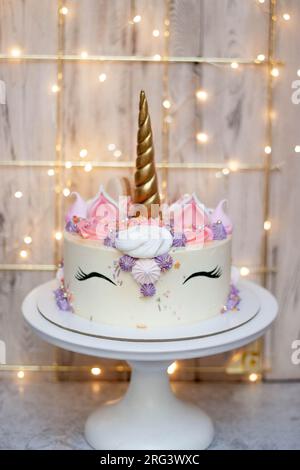 Gâteau licorne avec corne fondante dorée, cils et glaçage au fromage à la crème sur fond de bokeh festif Banque D'Images