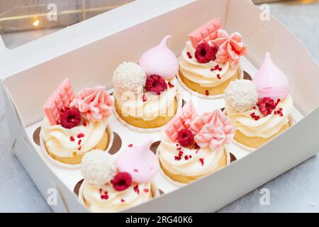 Coffret cadeau avec de beaux cupcakes roses décorés de mini barres de chocolat, meringue, framboise et fromage à la crème glaçage Banque D'Images