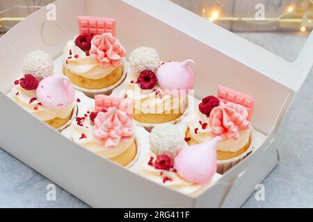 Coffret cadeau avec de beaux cupcakes roses décorés de mini barres de chocolat, meringue, framboise et fromage à la crème glaçage Banque D'Images