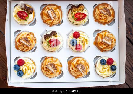 Cupcakes assortis dans une boîte cadeau avec fraises fraîches, beurre de cacahuète, caramel argenté, chocolat, framboise, fraise et myrtille Banque D'Images