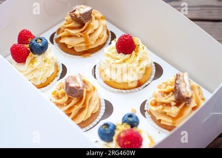 Cupcakes assortis dans une boîte cadeau avec fraises fraîches, beurre de cacahuète, caramel argenté, chocolat, framboise, fraise et myrtille Banque D'Images