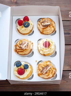 Cupcakes assortis dans une boîte cadeau avec fraises fraîches, beurre de cacahuète, caramel argenté, chocolat, framboise, fraise et myrtille Banque D'Images