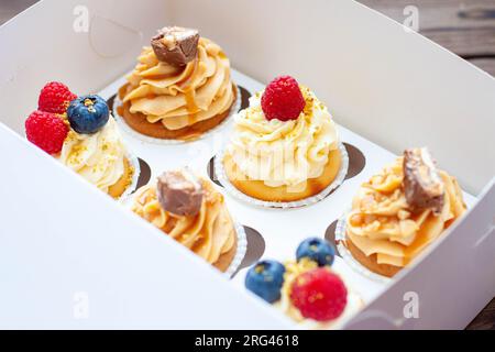 Cupcakes assortis dans une boîte cadeau avec fraises fraîches, beurre de cacahuète, caramel argenté, chocolat, framboise, fraise et myrtille Banque D'Images